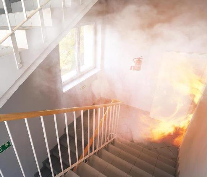Stairway filled with smoke with fire burning through a doorway.